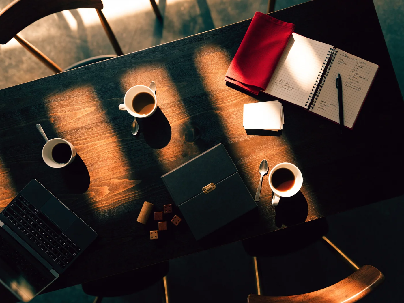 A table from above with a notebook of plans, blank name cards, a laptop, coffee and a board game
